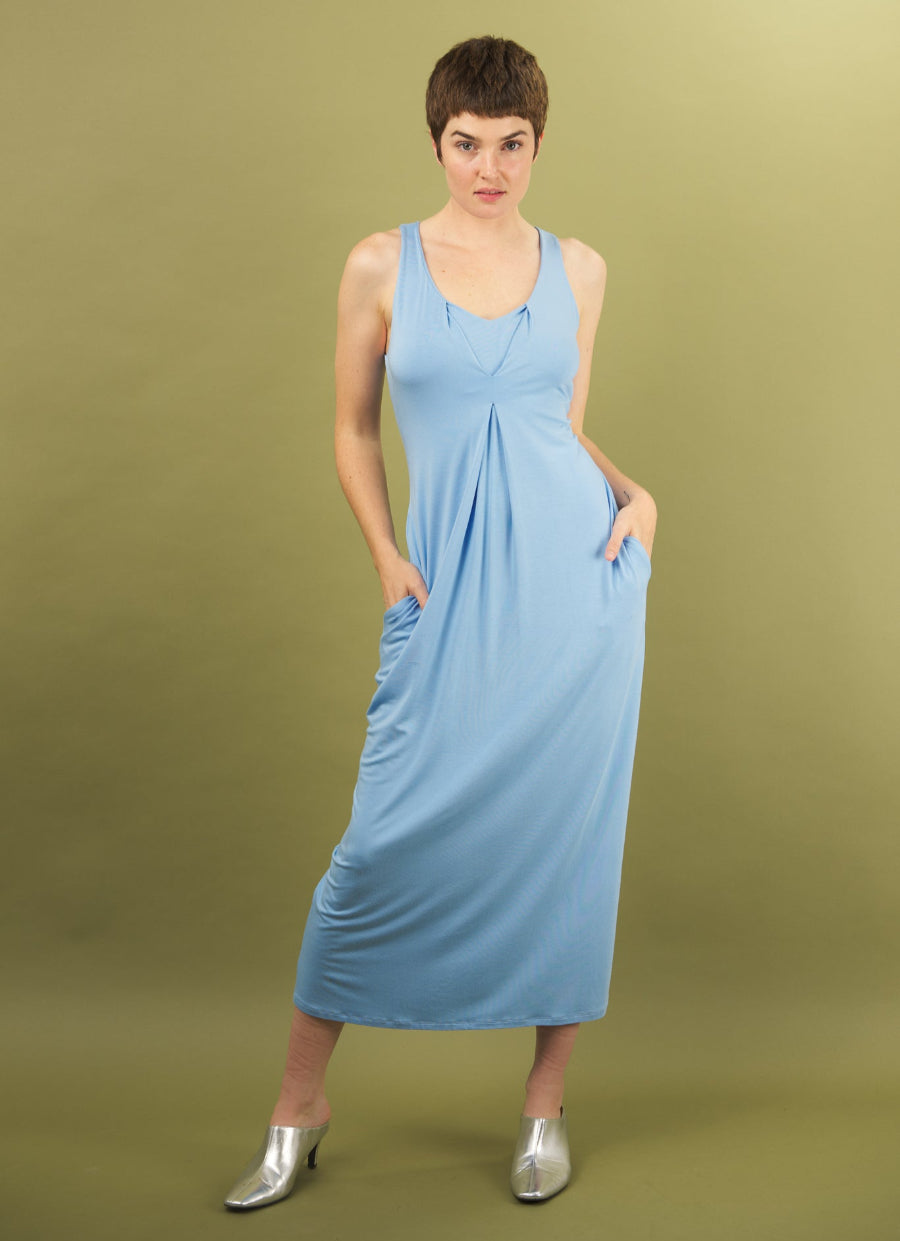 Woman wearing a sky blue royal tuck dress by inlarkin against an olive green background