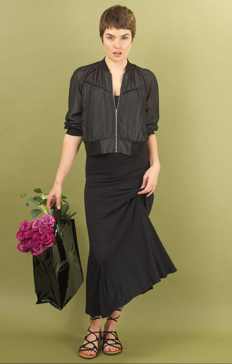 Woman in black sharyn dress and beauty bomber by inlarkin holding flowers against a green background