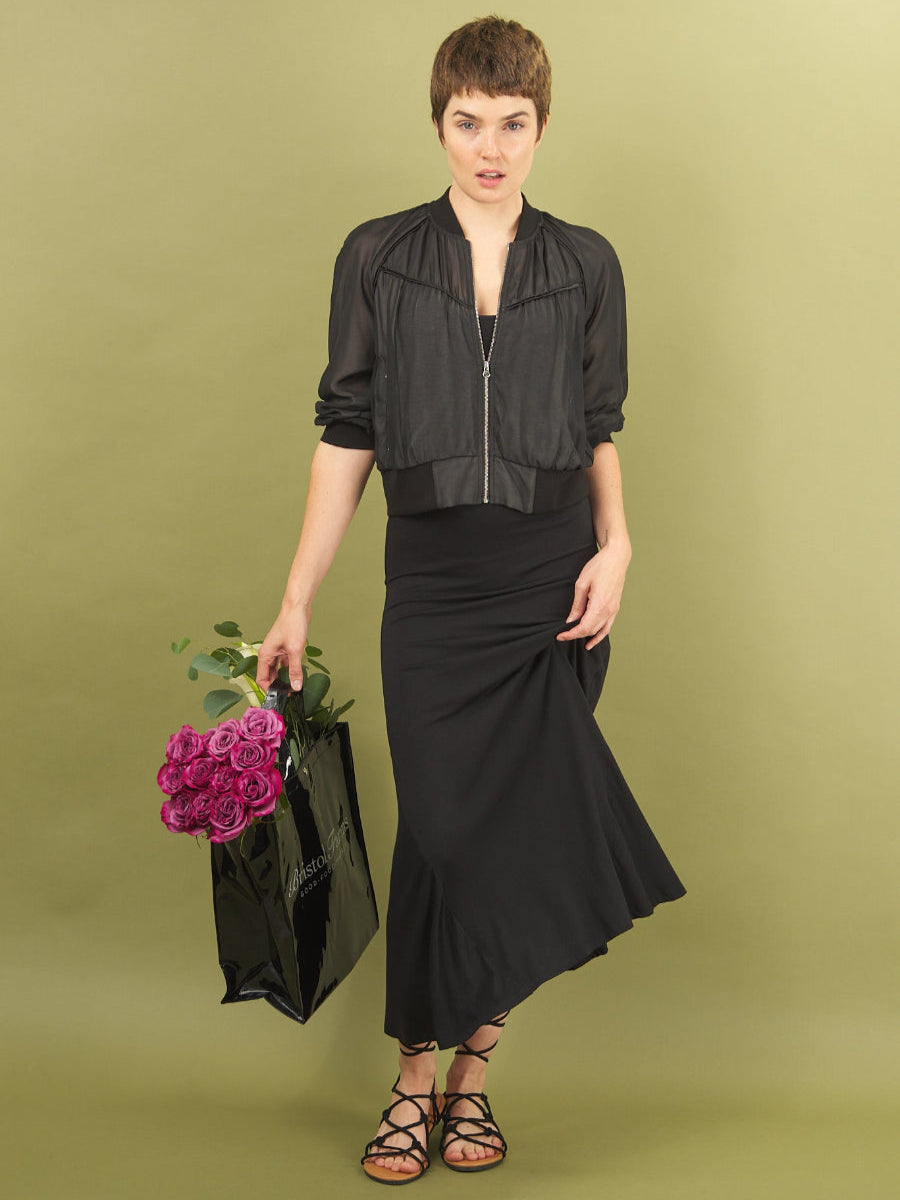 Woman in black sharyn dress and beauty bomber by inlarkin holding flowers against a green background