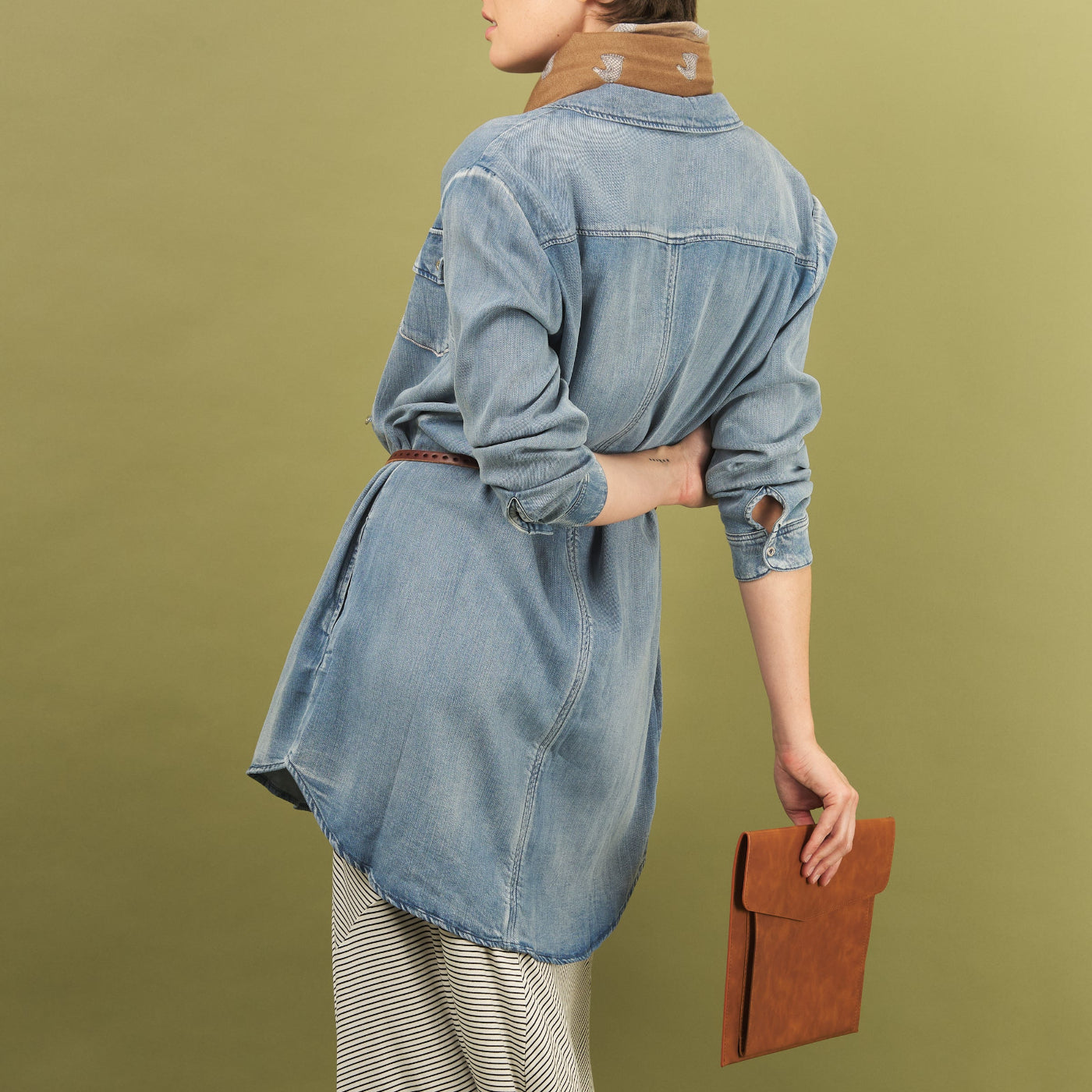 woman wearing a blue sy denim shirt by inlarkin holding a brown clutch against a green background