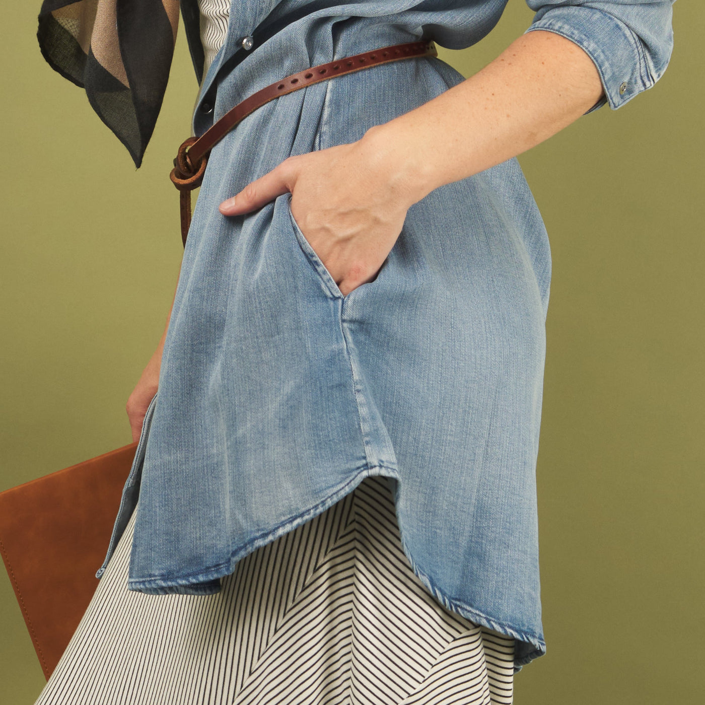 woman wearing a denim sy shirt by inlarkin showing the side pocket detail against a green background 