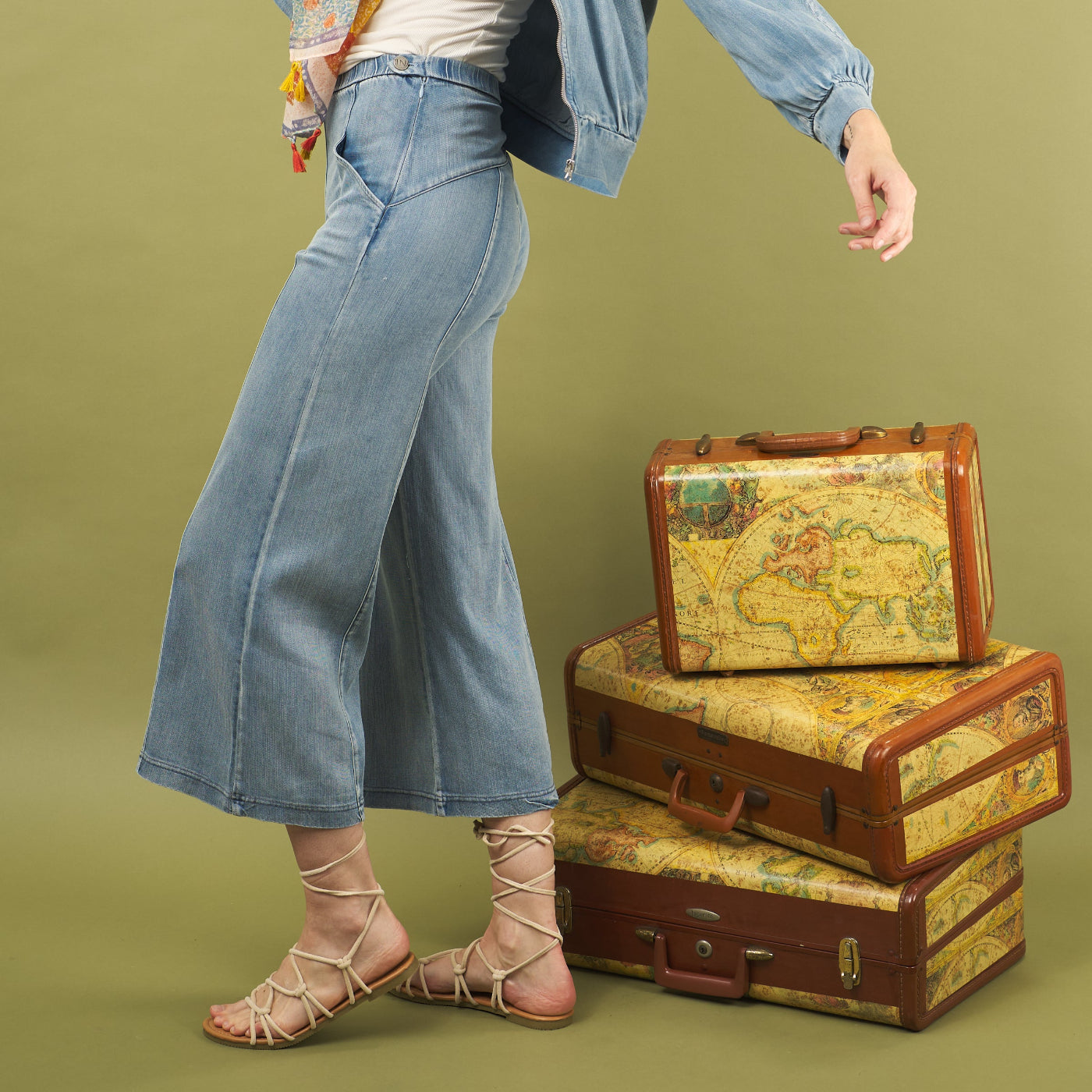 woman wearing the whitley jean by inlarkin jstanding next to vintage suitcases with world map designs on a green background