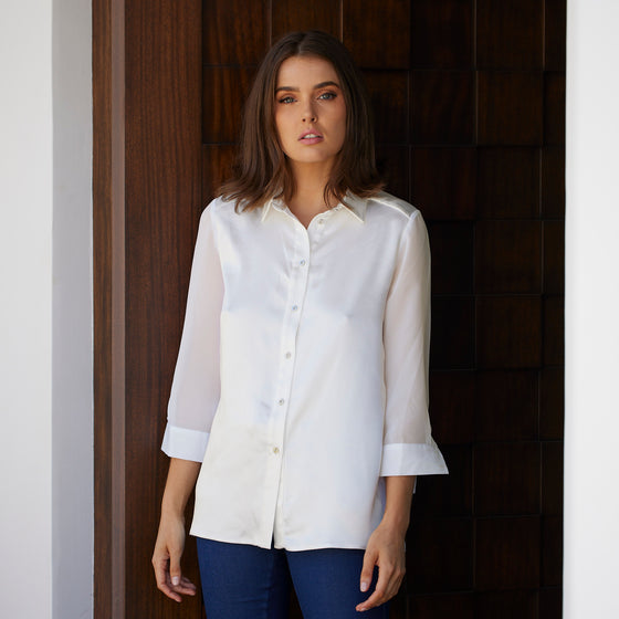 woman standing in the door wearing a white buttoned up aliferous shirt by inlarkin showing the button detail, bracelet sleeve length and sheer sleeve detail