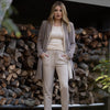 woman standing in front of a wood pile outdoors wearing pebble cashmere blend joggers and a cashmere cardigan with long taupe boy blazer, all pieces by inlarkin